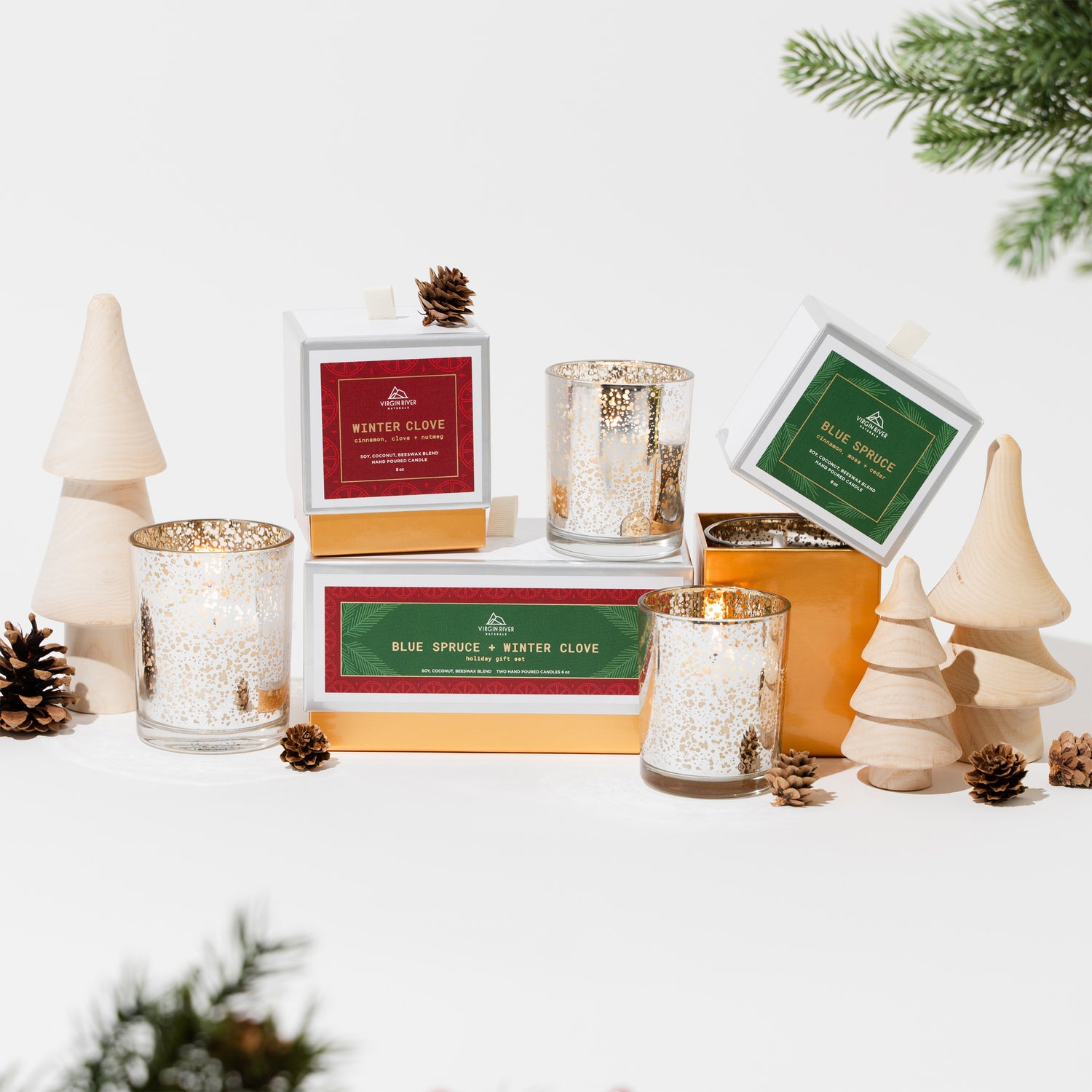 Holiday Blue Spruce and Winter Clove candles in antiqued glass jars surrounded by pinecones and decorative mini Christmas trees