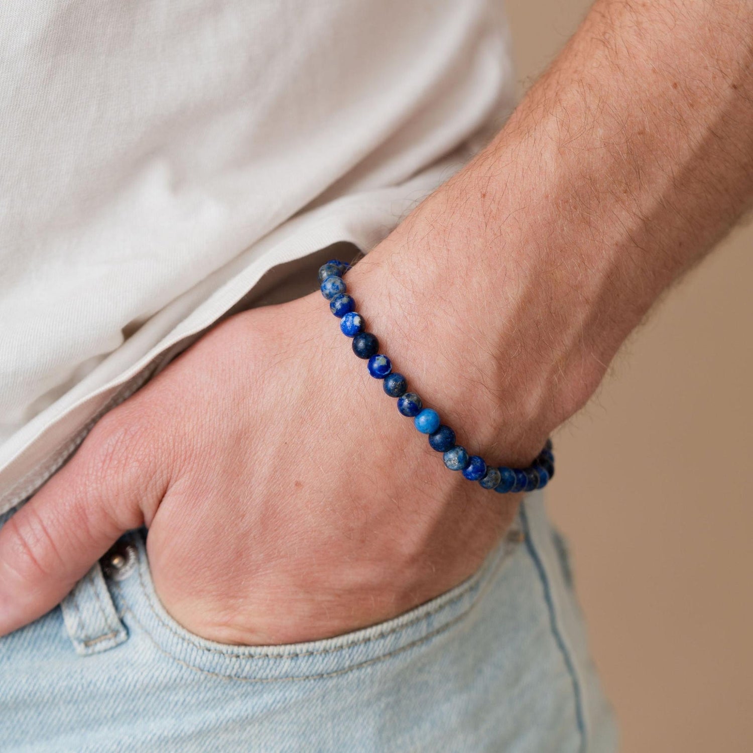 A person wearing a blue beaded bracelet with their hand in a pocket of light blue jeans